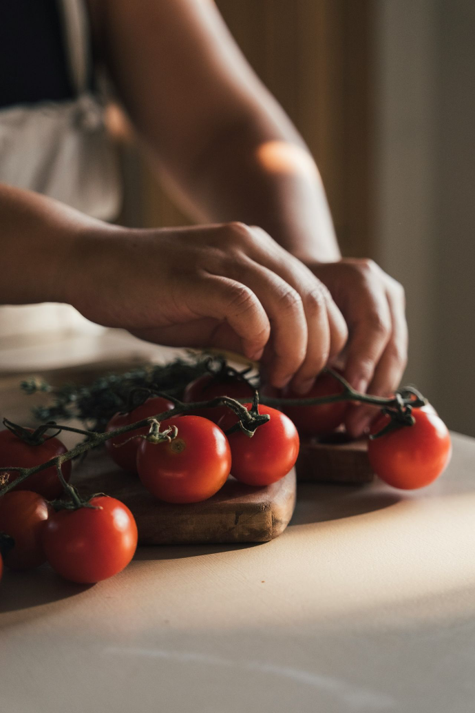 Hands arranging fresh cherry tomatoes on a wooden board